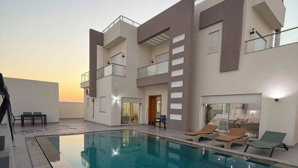 A modern building with a swimming pool, outdoor seating, and a balcony. - Villa Younes (Djerba Midun)