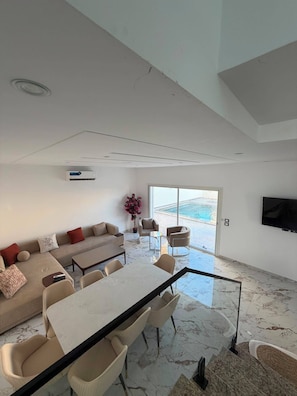 A modern living room with a sofa, dining table, chairs, and a TV.