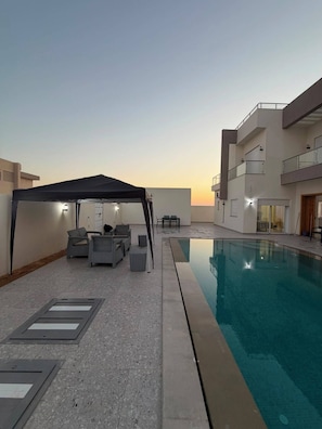 Un área de piscina en la azotea con zona de estar cubierta y vistas despejadas al atardecer.