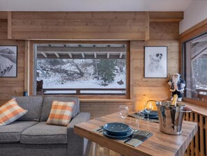 A cozy room with a wooden ceiling, a sofa with plaid cushions, a dining table set with plates and a champagne bucket, and framed pictures on the walls. - Le Petit Megève, with panoramic views and a 10-minute walk from downtown (Megève)
