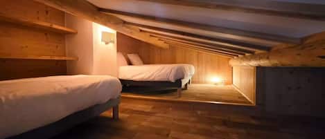 A cozy attic bedroom with two beds, wooden beams, and a sloped ceiling.