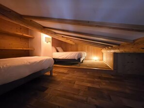 Um quarto de sótão aconchegante com duas camas, vigas de madeira e teto inclinado.