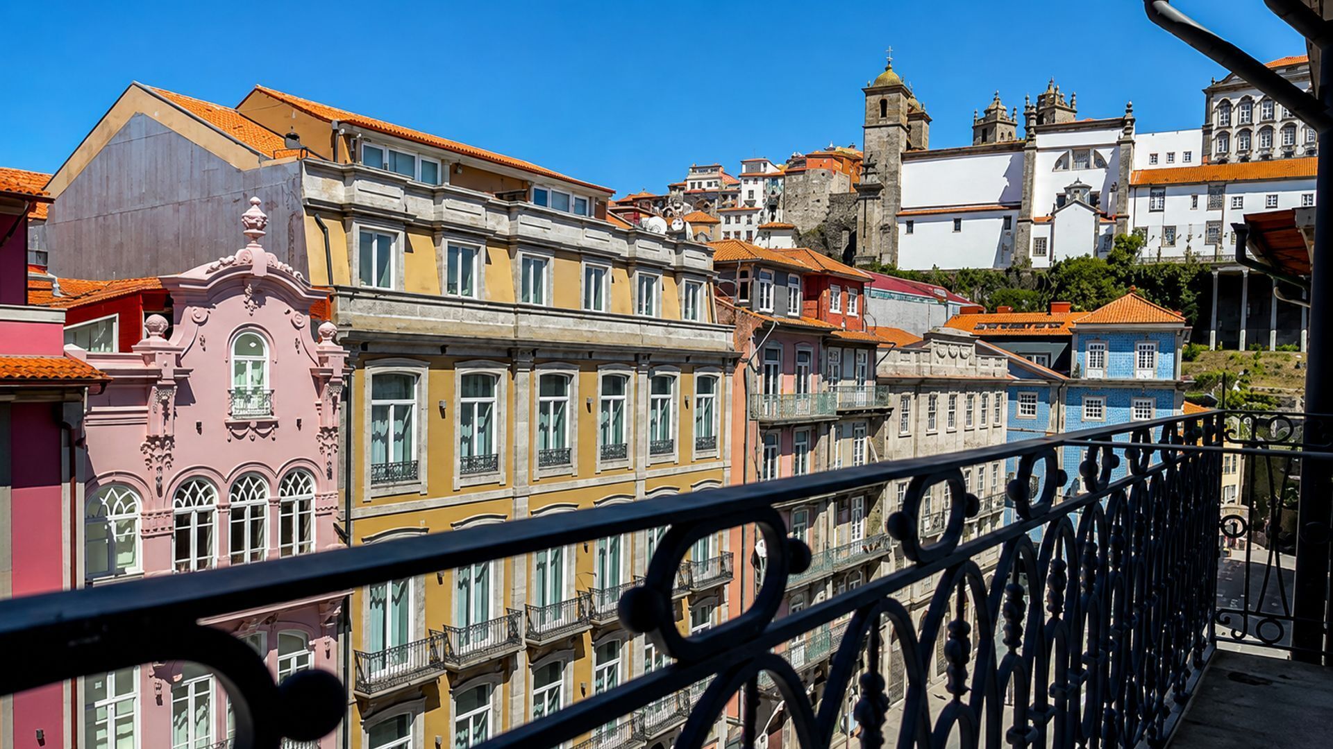 Varanda com grades de metal ornamentadas, vista para uma fileira de edifícios coloridos com diferentes estilos arquitetônicos.
