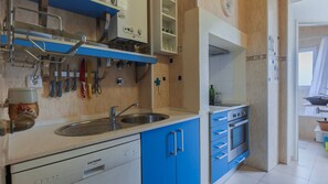 Een keuken met blauwe kastjes, een vaatwasser en verschillende keukengerei dat aan de muur hangt.