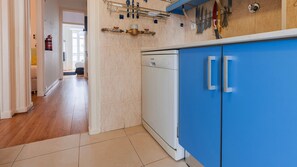 Een keuken met een vaatwasser, blauwe kastjes en een betegelde vloer.