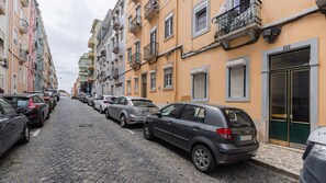 A cobblestone street lined with parked cars and multi-story buildings with balconies. - Arroios City Base | 2BR & Workspace by LovelyStay (Lisboa)
