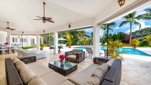 Ein überdachter Außenbereich mit Sofas, einem Couchtisch und einem Pool im Hintergrund.
