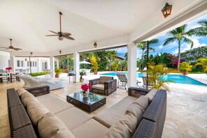 Ein überdachter Außenbereich mit Sofas, einem Couchtisch und einem Pool im Hintergrund.
