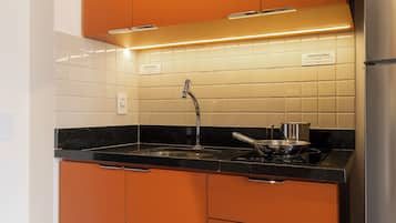 Cozinha com armários laranja, geladeira de aço inoxidável, bancada preta e painel de azulejos.