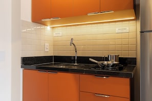 Eine Küche mit orangefarbenen Schränken, einem Edelstahlkühlschrank, einer schwarzen Arbeitsplatte und einer gefliesten Spritzschutzwand.