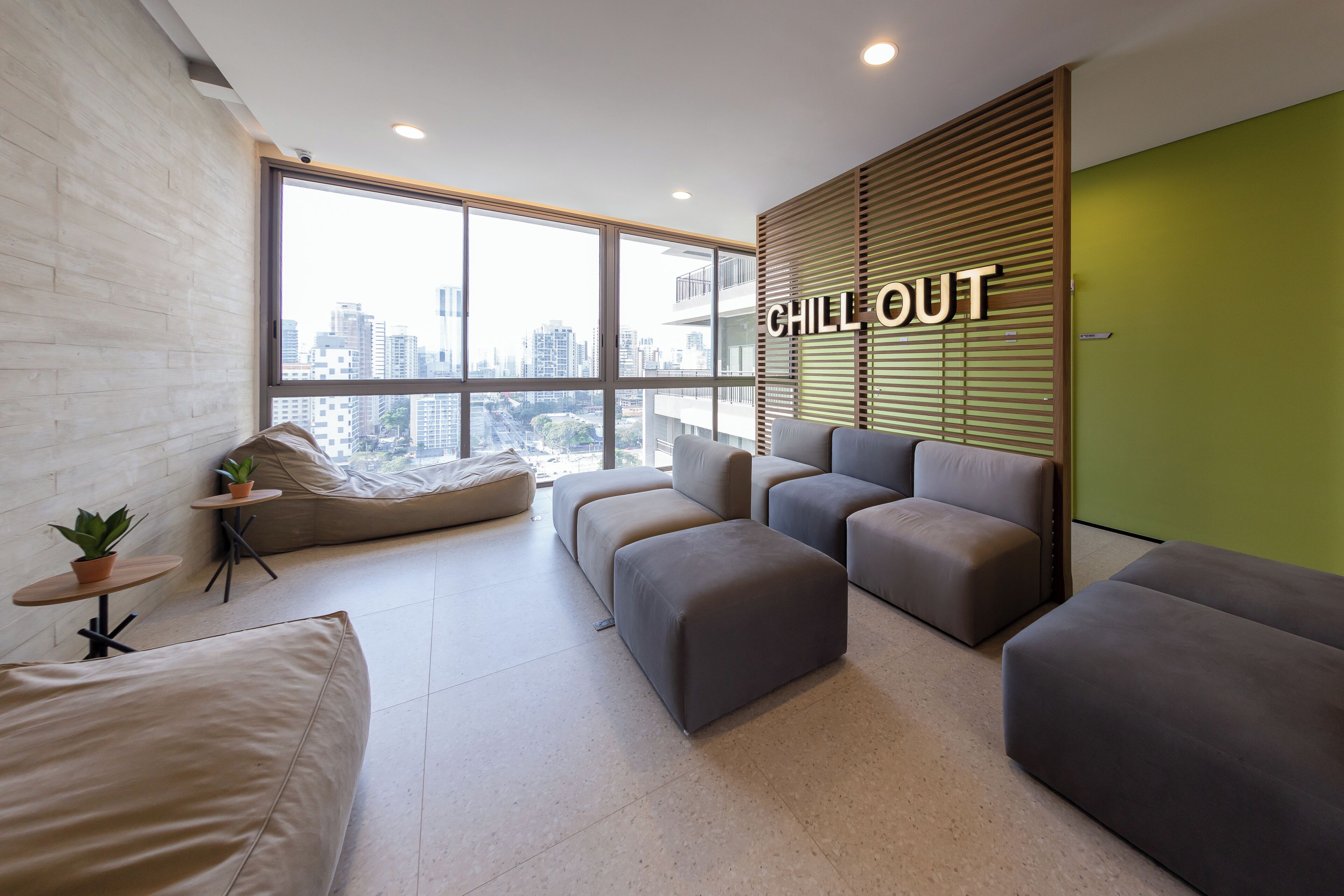 Uma área de estar moderna com vista para a cidade, um letreiro com a inscrição 'CHILL OUT' e uma parede verde de destaque.