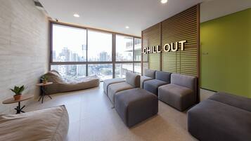 Uma área de estar moderna com vista para a cidade, um letreiro com a inscrição 'CHILL OUT' e uma parede verde de destaque.