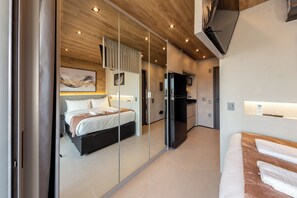 Ein modernes Schlafzimmer mit einem großen Bett, einem eingebauten Kleiderschrank und einer Küchenzeile inklusive Kühlschrank und Mikrowelle.