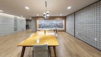 Uma sala de conferências moderna com uma longa mesa de madeira, cadeiras, um vaso de plantas e uma grande janela com vista para a cidade.