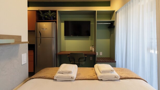 Ein Hotelzimmer mit einem Bett, einem Schreibtisch, einem Sessel, einem Fernseher und einem Kühlschrank.