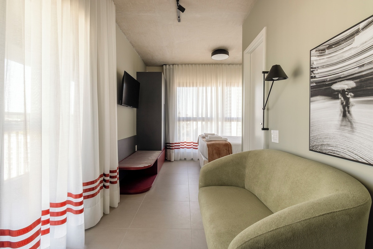 A hotel room with a bed, a sofa, a TV, and a painting on the wall.
