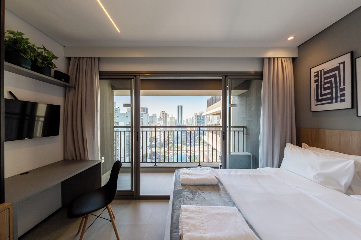 A modern hotel room with a balcony, a bed, a desk, and a chair.