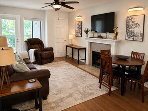 A living room with a fireplace, a ceiling fan, a TV mounted above it, and a dining area with a table and chairs. - Downtown Gatlinburg / 2 King Suites / Pool+Hot Tub (Gatlinburg)