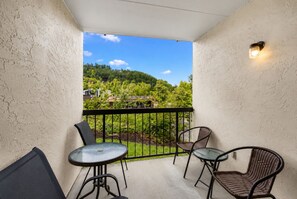 A balcony with a glass table, two wicker chairs, and a view of a green landscape. - Downtown Gatlinburg / 2 King Suites / Pool+Hot Tub (Gatlinburg)