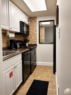 A kitchen with white cabinets, a black stove, a microwave, and a refrigerator. - Downtown Gatlinburg / 2 King Suites / Pool+Hot Tub (Gatlinburg)