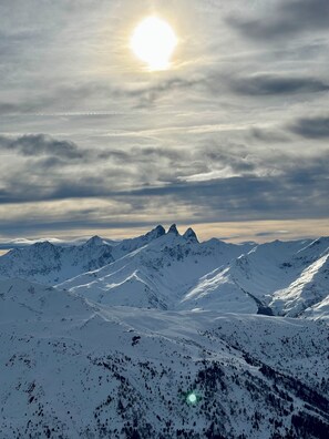 A snow-covered mountain range with a clear sky and the sun visible.