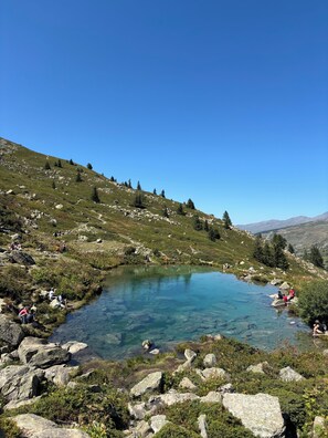 A clear mountain lake surrounded by rocky terrain and sparse vegetation.