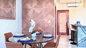 A dining area with a round glass table, brown chairs, and a decorative wall with geometric patterns. - Walk 2 Fun, Beaches, Dining, Shopping, Nightlife (Punta Cana)