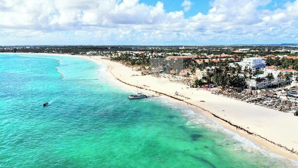 A coastal view with a beach, a boat, and buildings in the distance. - Walk 2 Fun, Beaches, Dining, Shopping, Nightlife (Punta Cana)