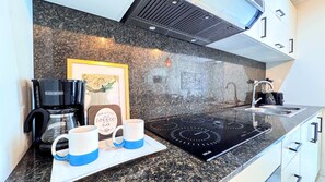 Eine Küche mit einer Kaffeemaschine, zwei Tassen, einem gerahmten Bild und einem modernen Herd.