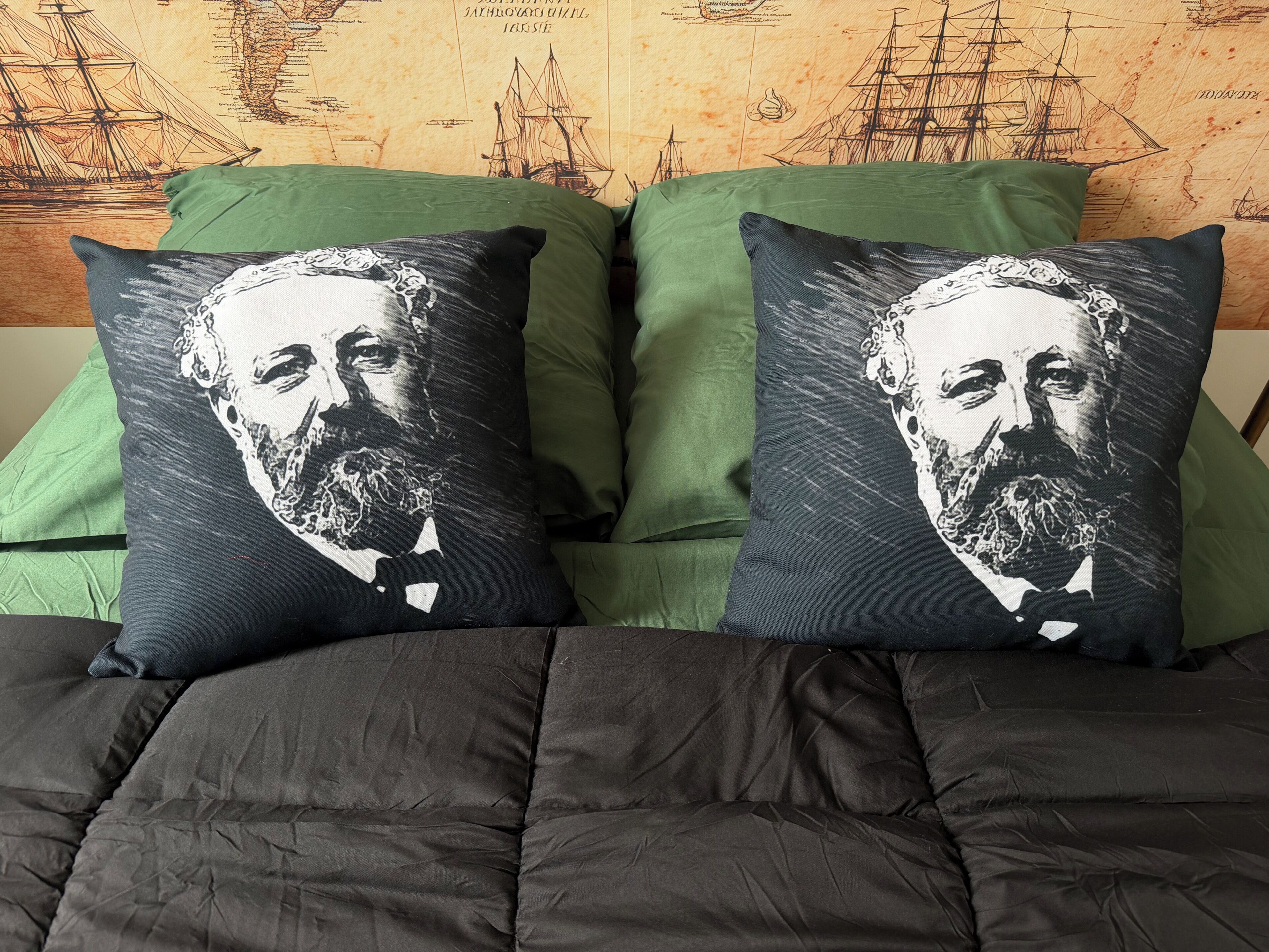 Een bed met een donkere quilt en twee sierkussens met een portretmotief.