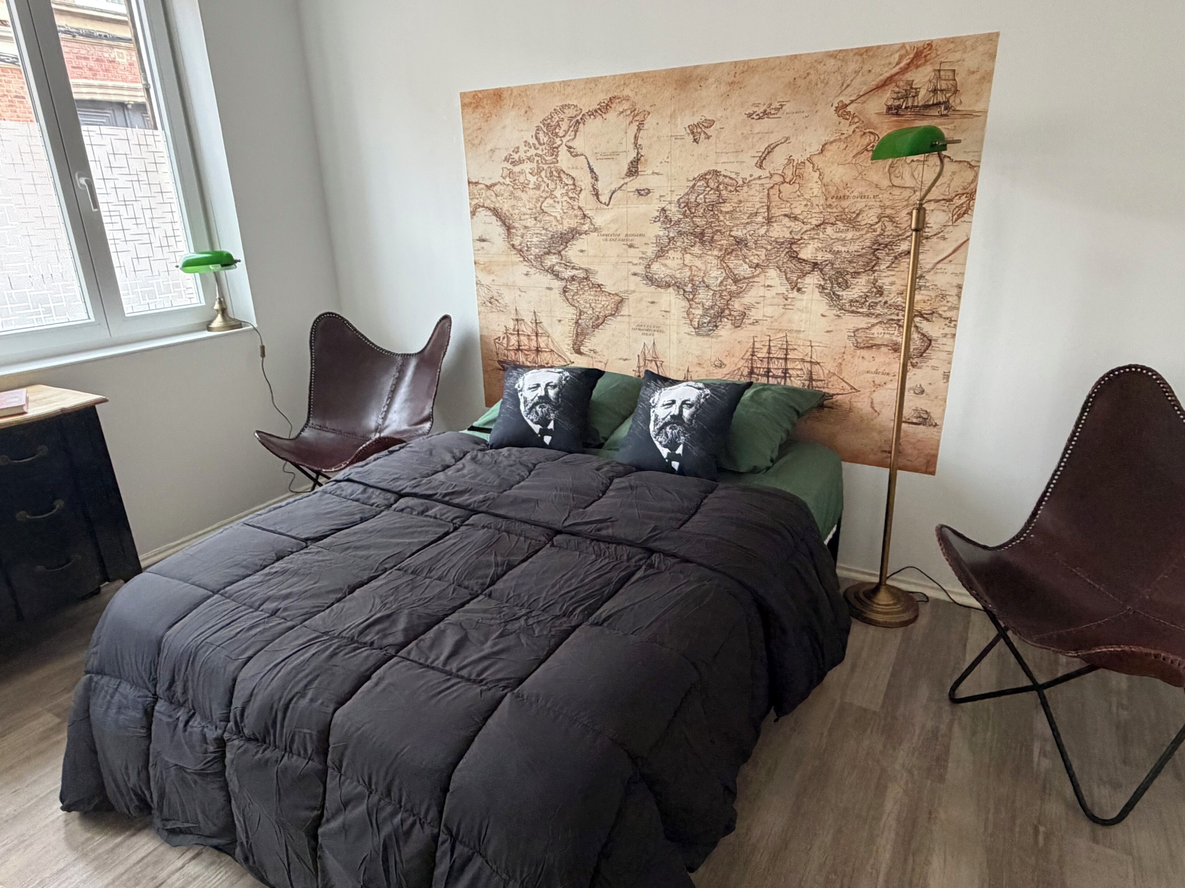 Een slaapkamer met een groot bed, een wereldkaart aan de muur, twee stoelen en een bureau.