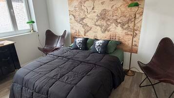 Een slaapkamer met een groot bed, een wereldkaart aan de muur, twee stoelen en een bureau.