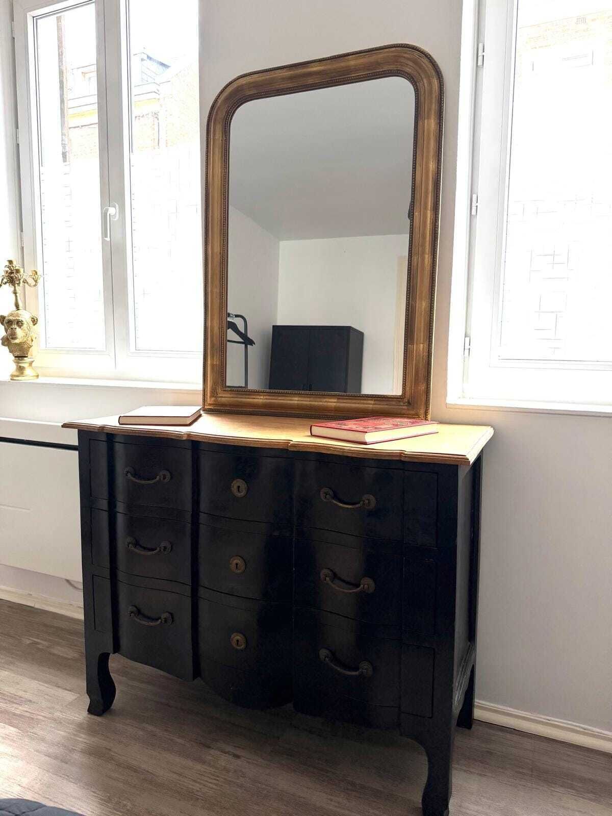 A dresser with a mirror, drawers, and a small vase with a plant on top.