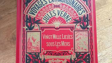Een boek met de titel 'Voyages Extraordinaires Jules Verne', met decoratieve illustraties en tekst.