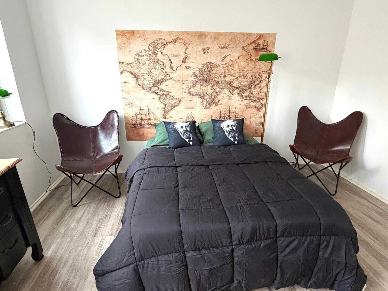 Ein Schlafzimmer mit einem großen Bett, zwei Ledersesseln, einer Karte an der Wand und einem Schreibtisch mit Lampe.