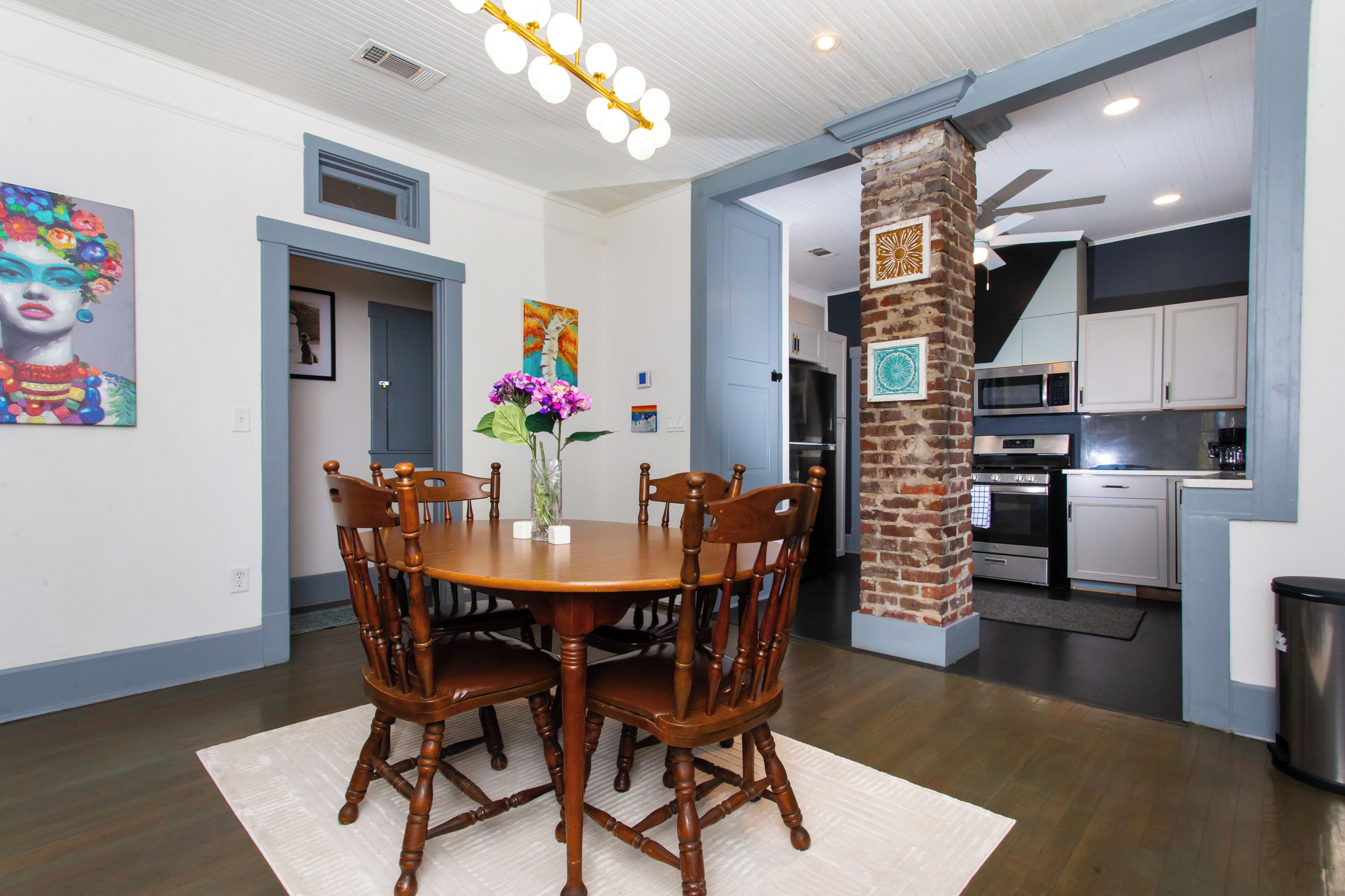 A dining area with a wooden table and chairs, a vase with flowers, and a brick column.