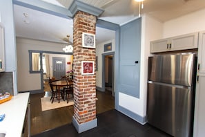 A kitchen with a brick pillar, stainless steel refrigerator, and a dining area with wooden chairs. - Charming 3BR/2BA Retreat West Downtown Pensacola (Pensacola)