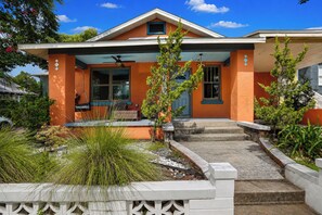 Ein zweistöckiges Haus mit Veranda, einem kleinen Garten und einem strahlend blauen Himmel.