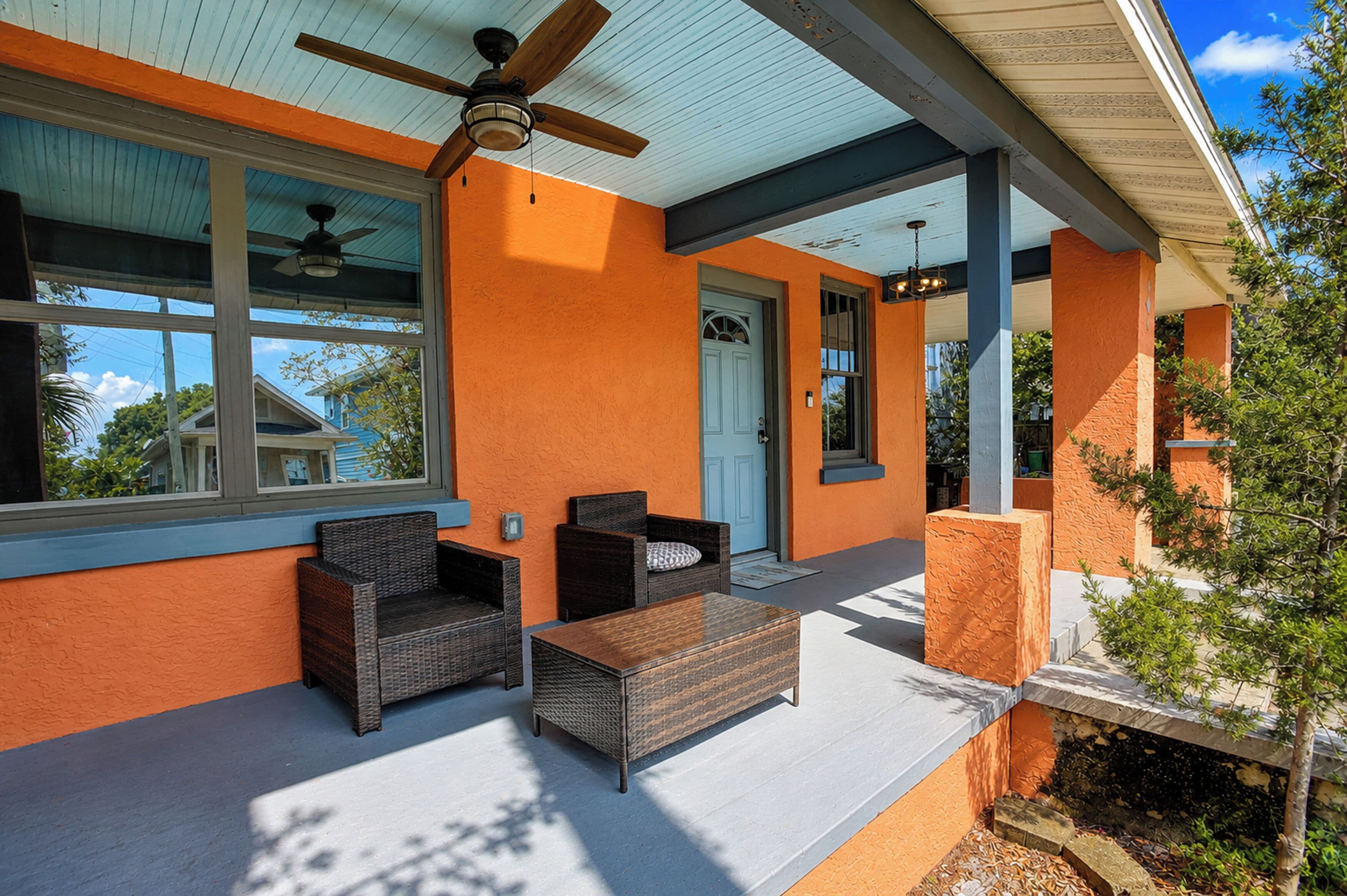 An outdoor seating area with wicker furniture, a ceiling fan, and a door leading to the interior.