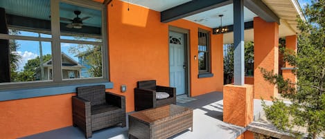 Un espace extérieur aménagé avec des meubles en osier, un ventilateur de plafond et une porte donnant accès à l’intérieur.