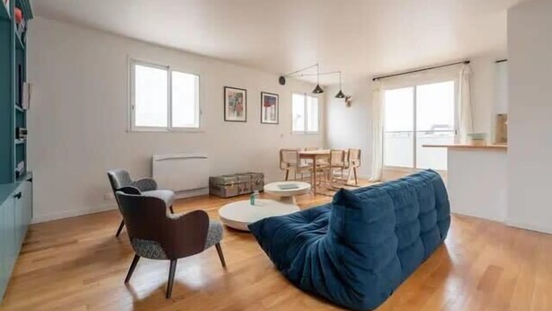 Uma sala de estar ampla com um sofá azul, uma mesa de centro redonda e uma mesa de jantar com cadeiras.