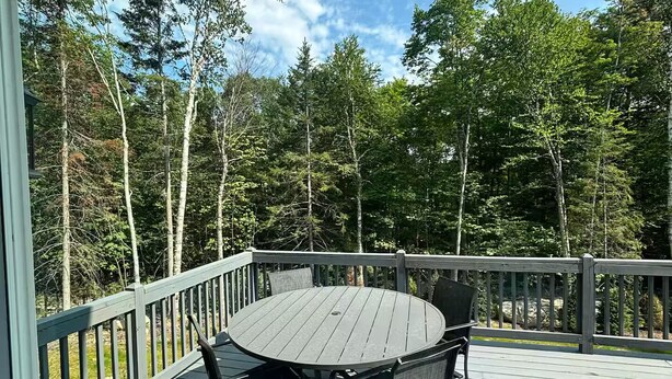 Eine Terrasse im Freien mit rundem Tisch und Stühlen, umgeben von einer Brüstung und Bäumen.