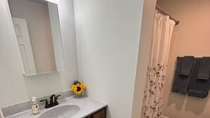 Ein Badezimmer mit Waschbecken aus Granit, einem Spiegel und einem blumigen Duschvorhang.