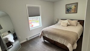 Ein Schlafzimmer mit Bett, einem Fenster mit Jalousien, einem Gemälde an der Wand und einer Deckenleuchte.