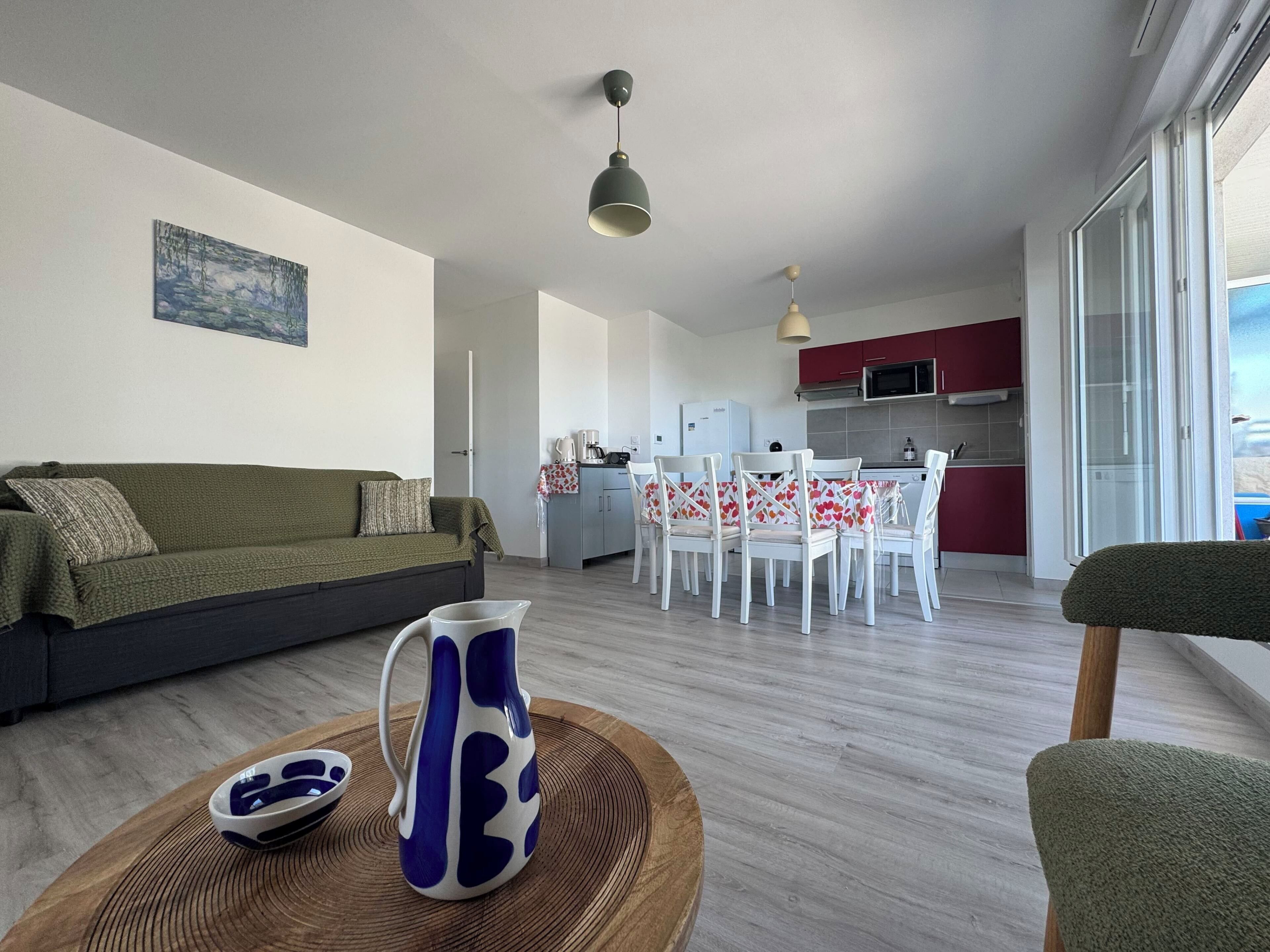 Ein Wohnzimmer mit einer Couch, einem Couchtisch mit einer Karaffe und einem Essbereich mit Stühlen und einem Tisch.