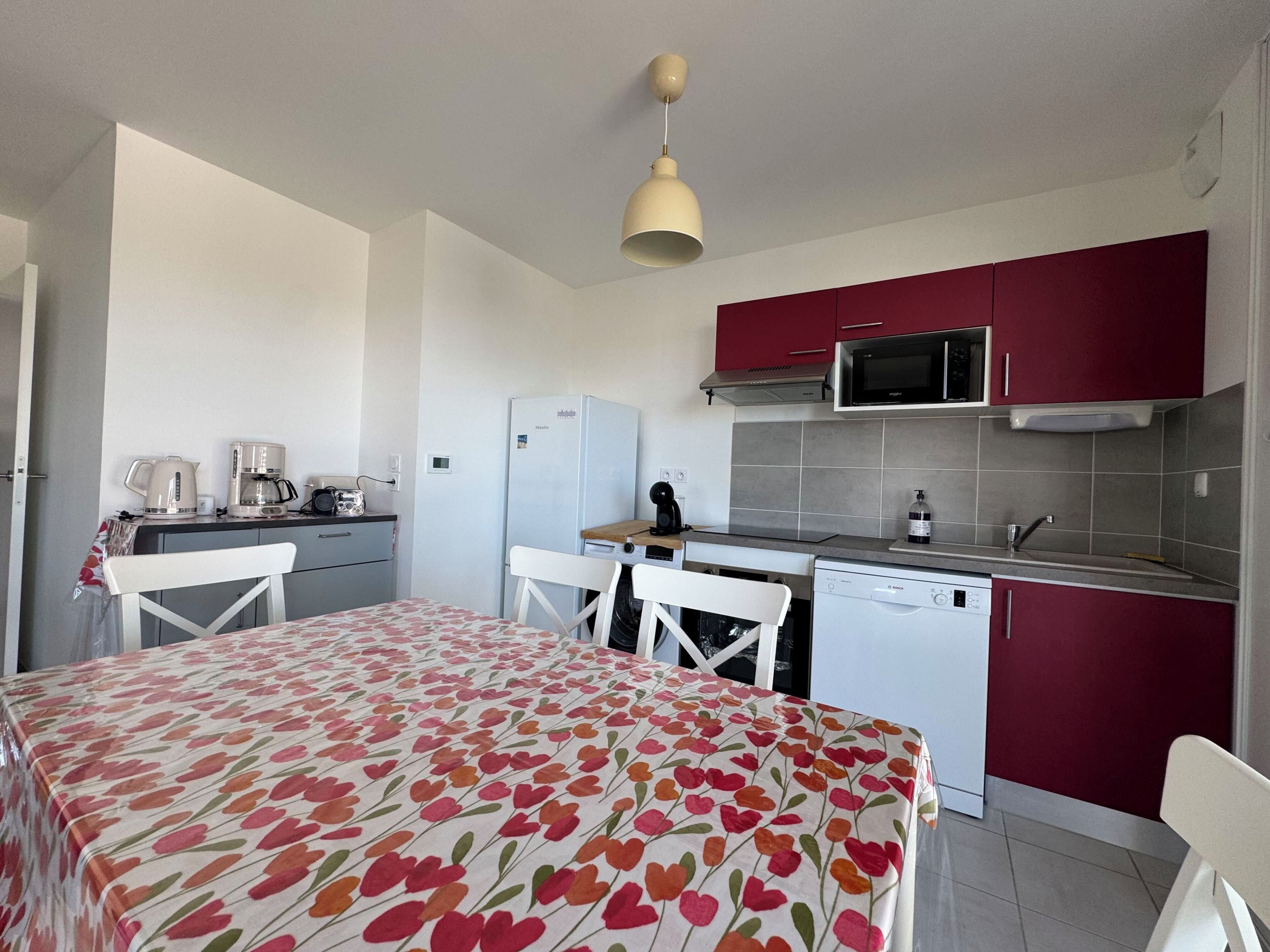 A compact kitchen with a refrigerator, microwave, and coffee maker. There is a dining area with a table and chairs.