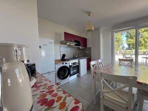 A compact kitchen with a washing machine, a microwave, and a dining area with a table and chairs. - 2-bedroom apartment with balcony, close to the sea (Cabourg)