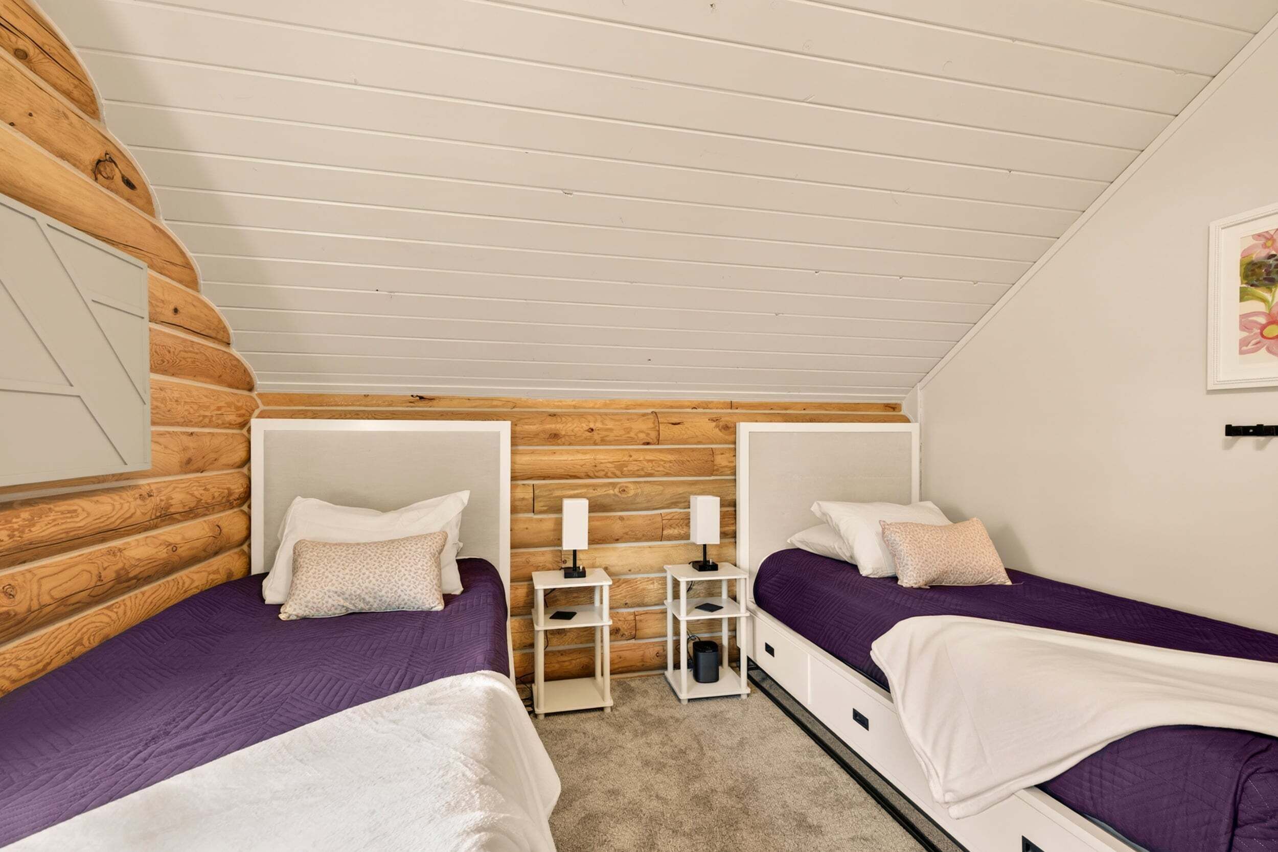 A room with two beds, wooden paneling on the walls, white ceiling, and a small table with lamps.