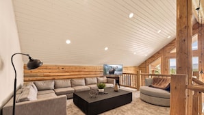 Ein gemütliches Blockhaus-Interieur mit einer Eckcouch, einem schwarzen Couchtisch, einem Fernseher und einem Holzbalkon.