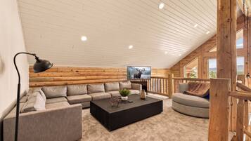 A cozy log cabin interior with a sectional sofa, a black coffee table, a TV, and a wooden railing.